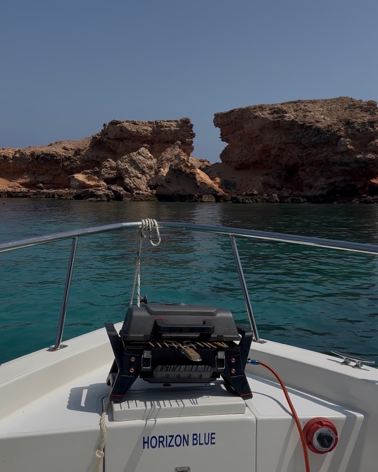 Bow of a Horizon Blue boat moored below the limestone cliffs of a Daymaniyat island